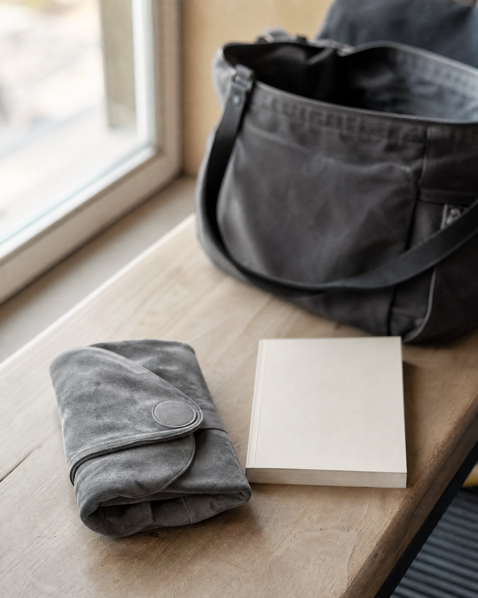 The grey NODD Travel Pillow folded flat next to a paperback book, in front of an open travel bag